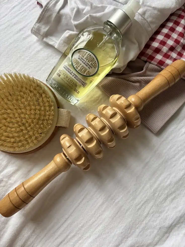 Rouleaux de bois de madérothérapie, brosse sèche et huile végétale sur un drap de lin.